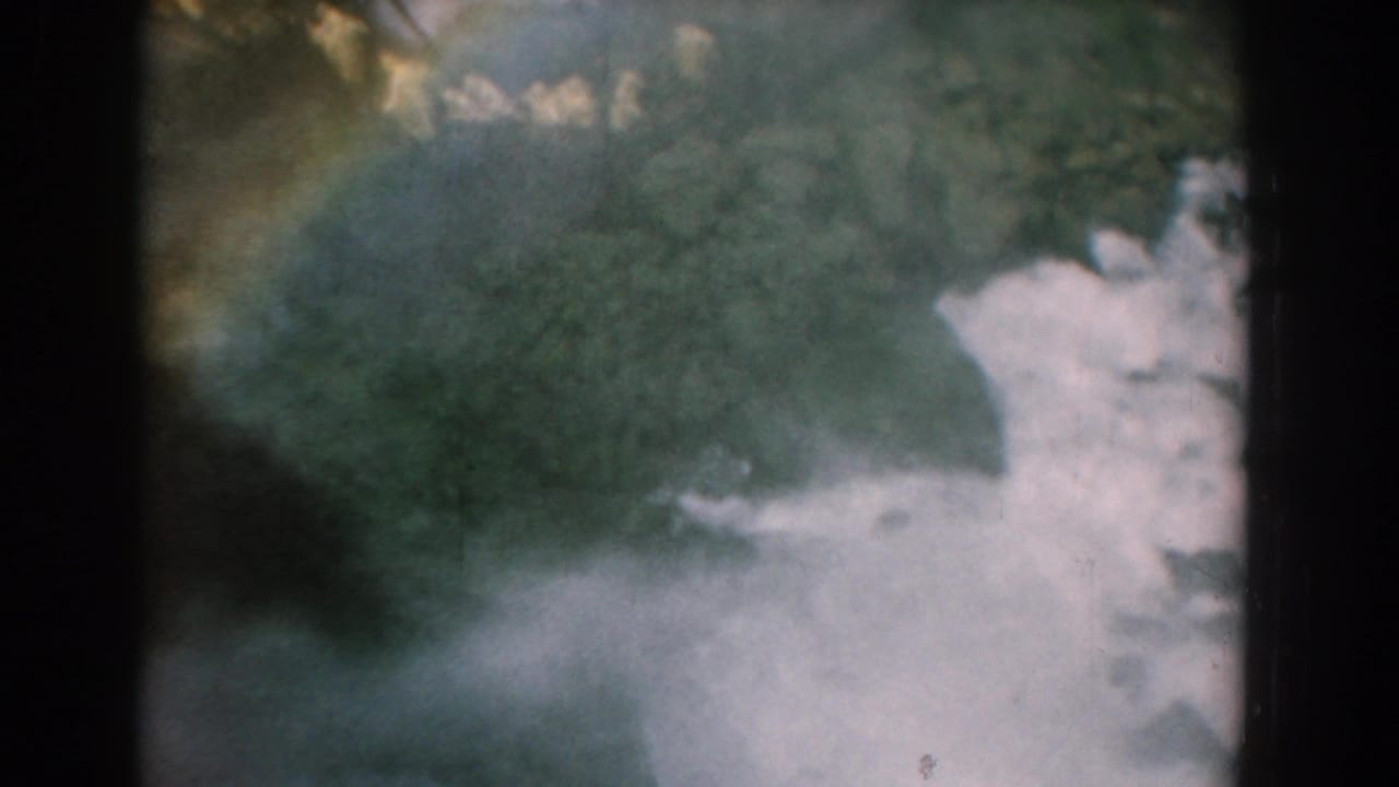 Rushing waterfall water and mist with dark rock shapes and a faint rainbow arc.