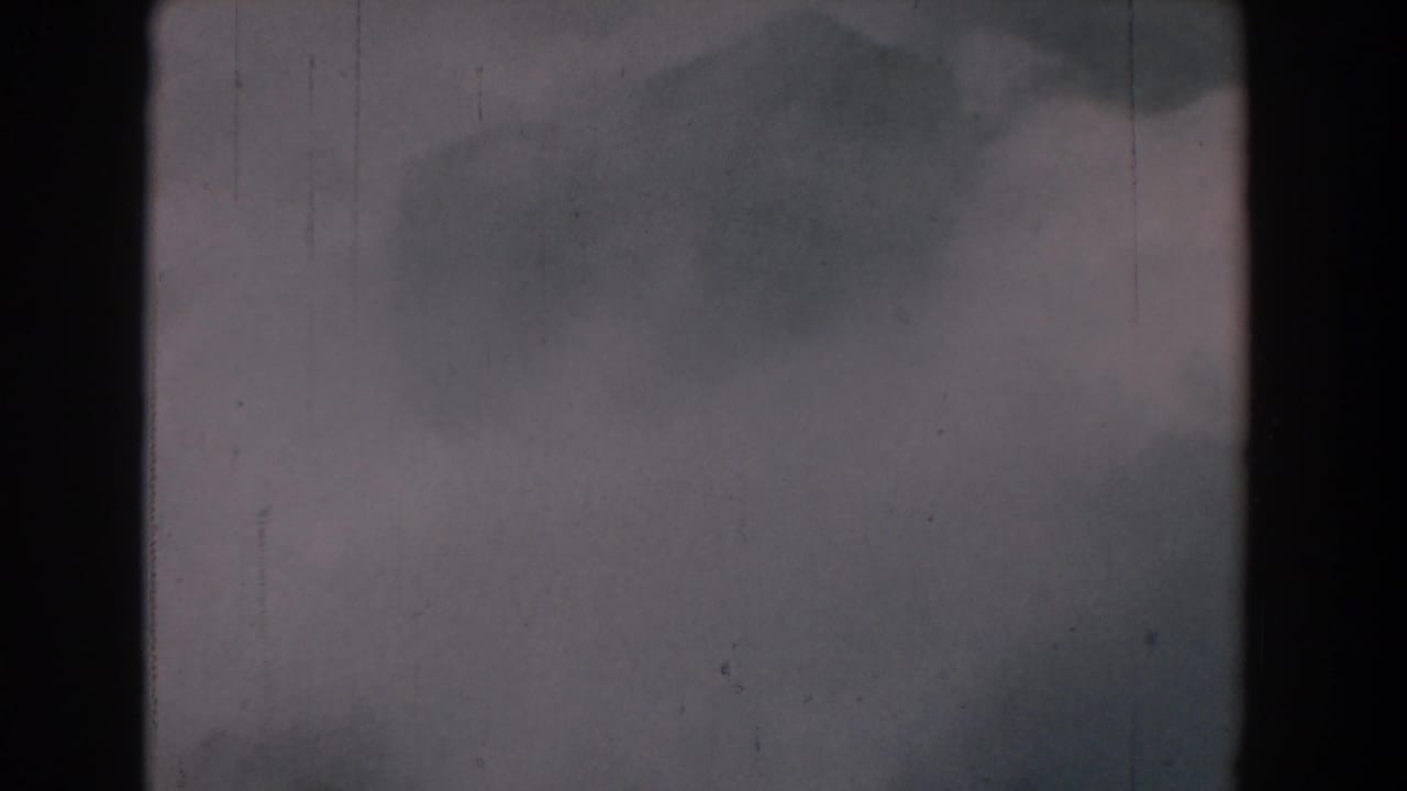 Soft gray mist and faint landscape forms within a scratched 8mm frame.