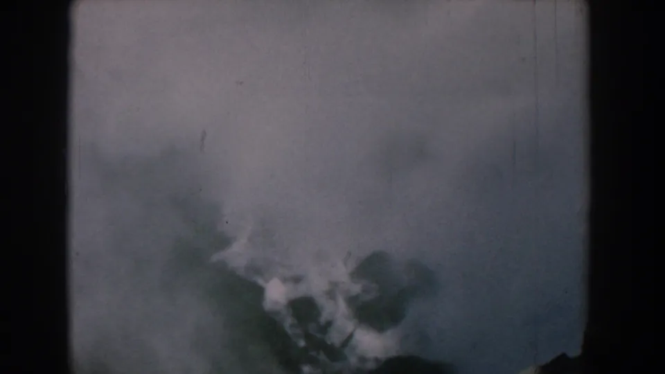 Yorktown, Virginia 1958 8mm frame with pale foamy water or spray beside dark rock-like shapes, haze, scratches, and dust.