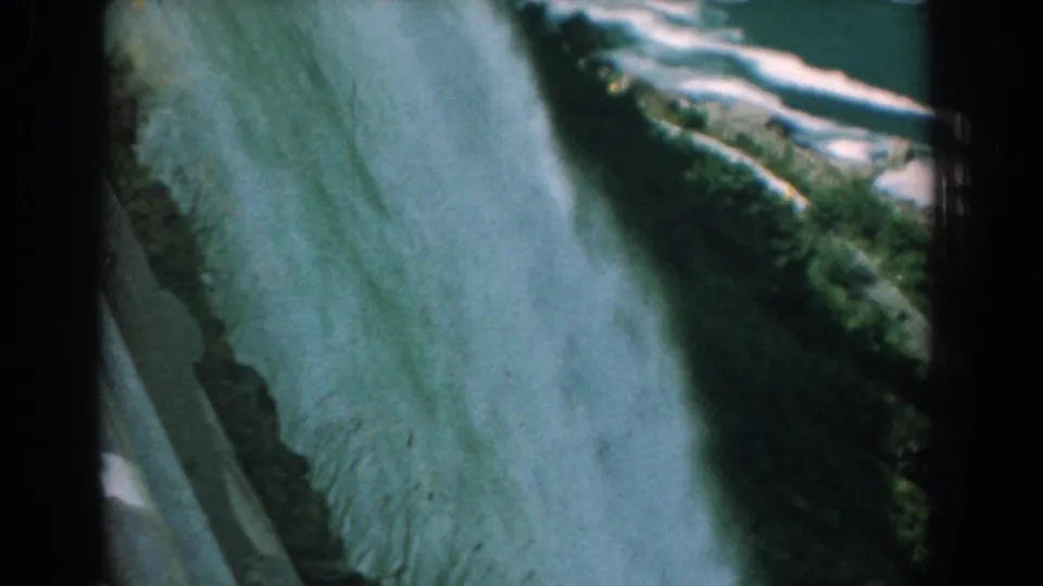 1958 8mm frame showing the falls plunging downward with whitewater, rocks, and green vegetation near the rim.