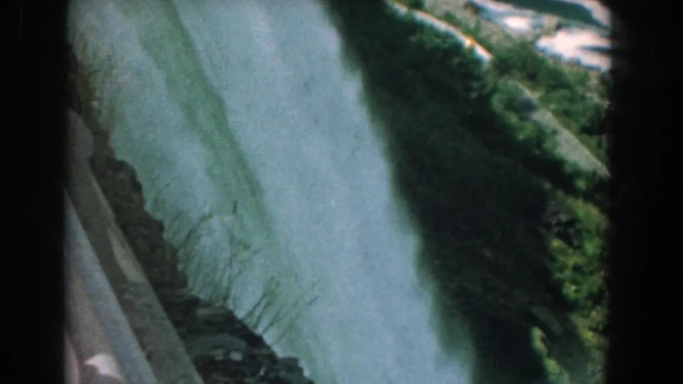 1958 8mm home-movie frame of rushing falls water beside a rocky, green ledge at Niagara Falls.