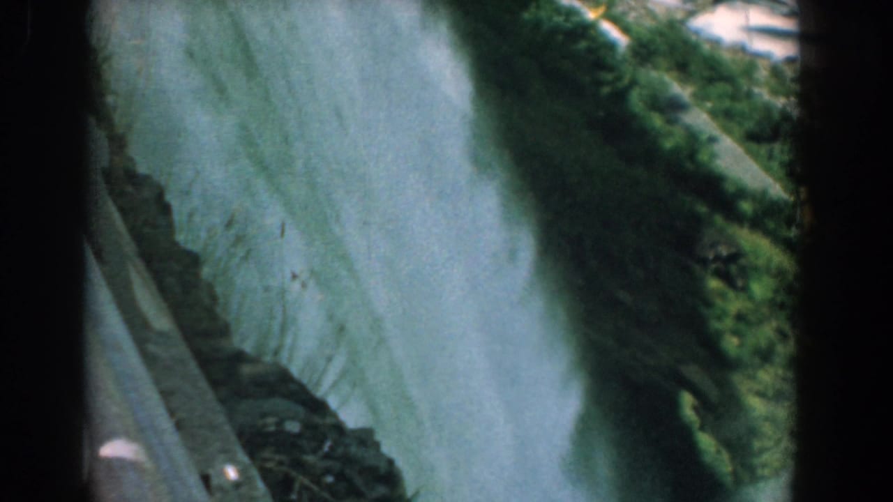 Misty waterfall beside dark rocks and green cliffside vegetation.