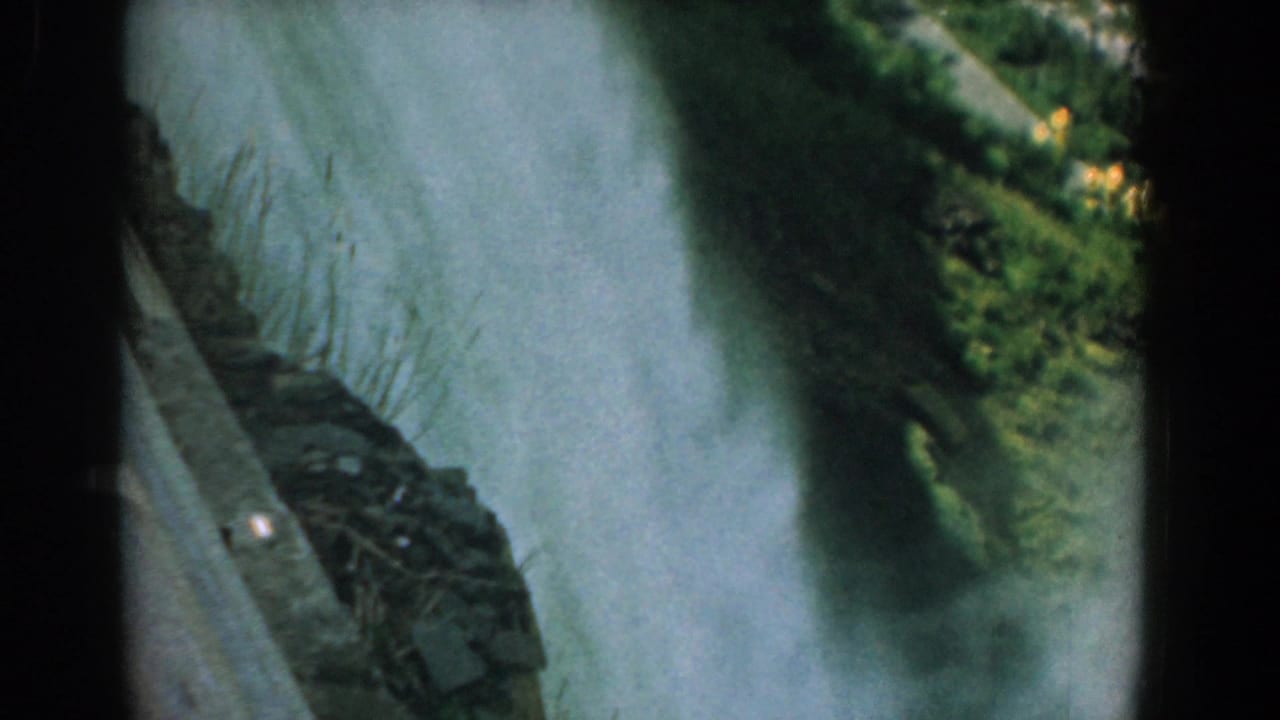 Waterfall spray fills the frame beside a rocky ledge and green trees.