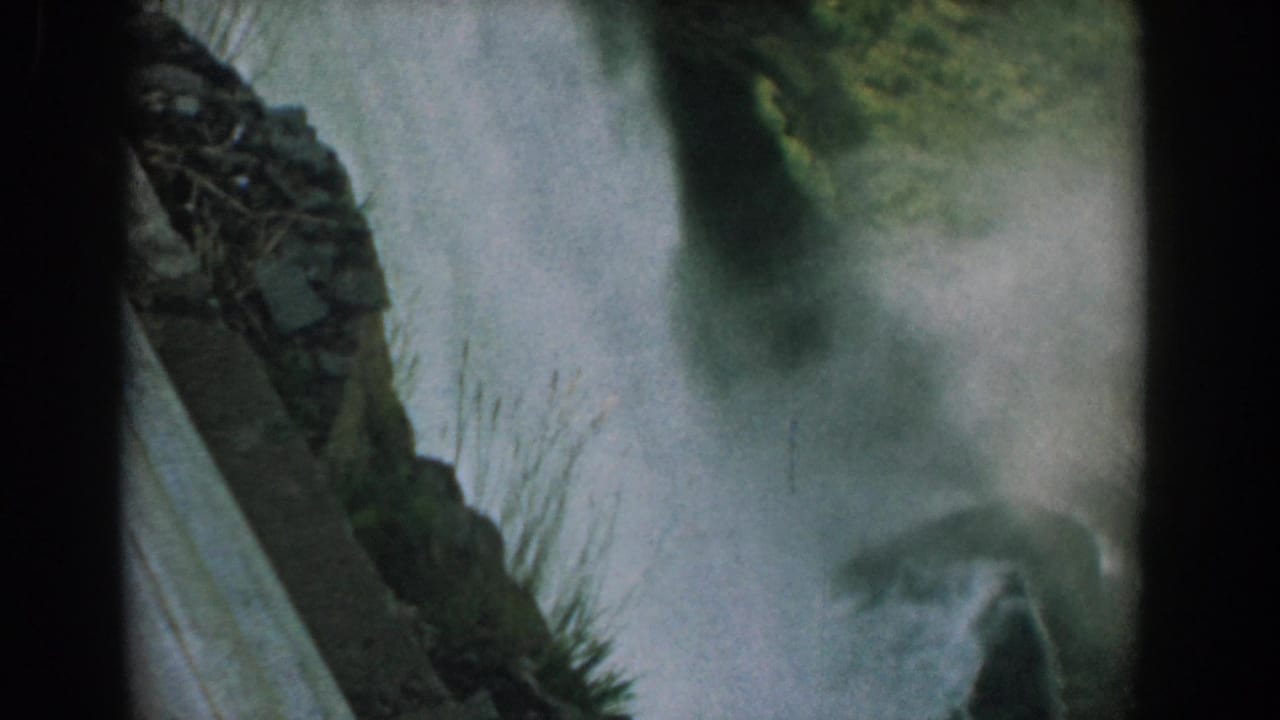 Misty waterfall seen beside dark rock and plants in a 1950s 8mm frame.
