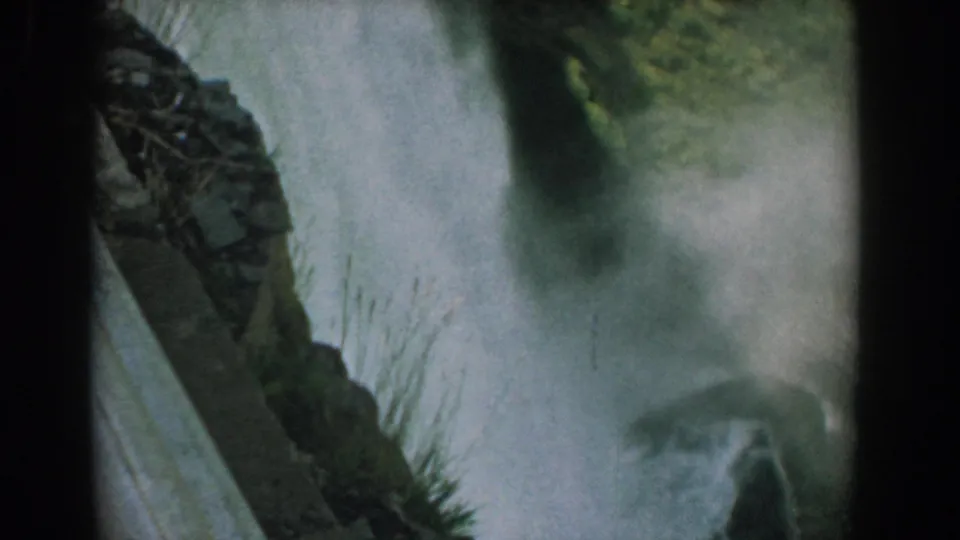1958 8mm view of Bridal Veil Falls at Niagara, with water dropping through mist beside dark rock and sparse vegetation.