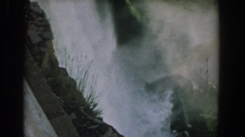 1958 Niagara Falls home-movie frame showing Bridal Veil Falls through heavy mist, with rock and greenery along the edge.