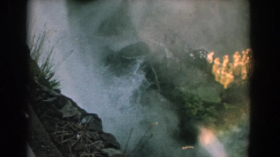 1958 Niagara home-movie frame showing mist around Bridal Veil Falls, with rocks, greenery, and indistinct raincoat-like shapes at right.