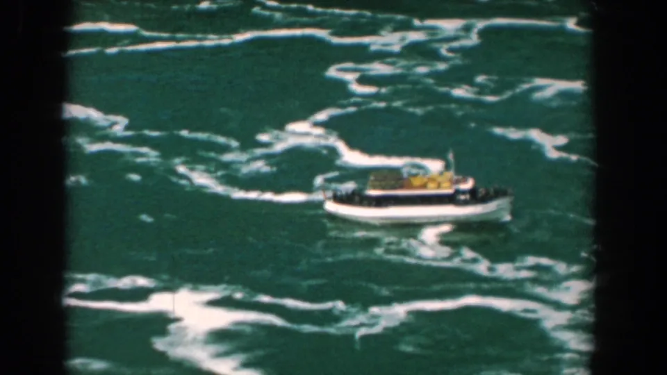 A small sightseeing boat travels across choppy water, framed by dark 8mm gate edges and visible film softness.