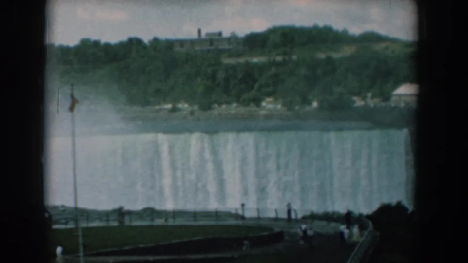 1958 8mm travel frame panning across the waterfall edge, with mist drifting below trees and visitors along the lower overlook.