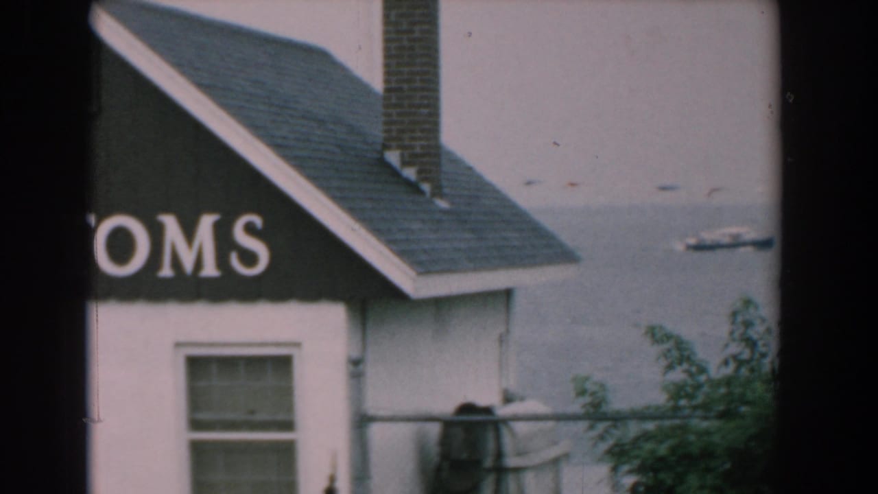 1958 Yorktown home-movie frame showing part of a CUSTOMS sign on a small building near calm water with a distant boat.