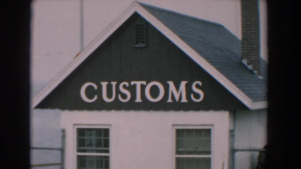 1958 Yorktown, Virginia home-movie frame showing a small white waterfront building with a dark CUSTOMS gable sign, windows, chimney, and railing.