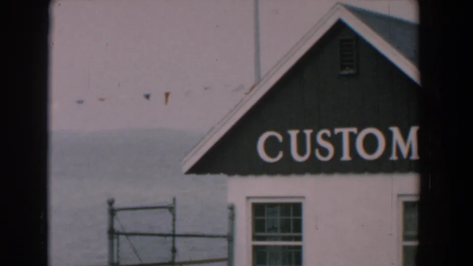 Late-frame 1958 Yorktown view of the customs-labeled building, tightly cropped with partial lettering, a window, railing, water, and pennant flags.