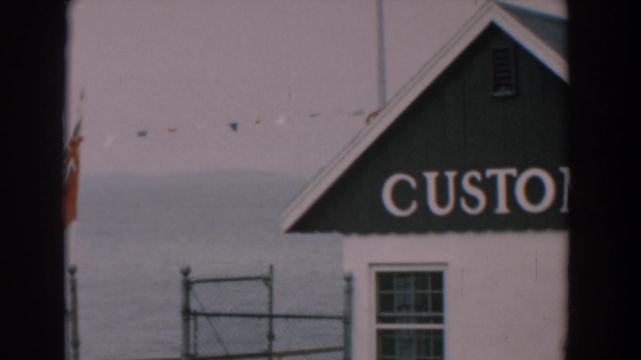 White waterfront building with partial CUSTOM sign, red flag, fence and water behind it.