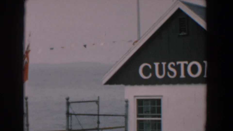 1958 Yorktown, Virginia 8mm frame showing a white waterfront building with partial CUSTOM lettering, a red flag, fence and calm water.
