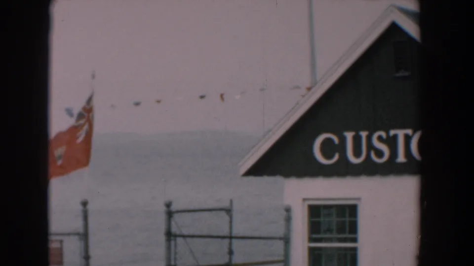 1958 Yorktown, Virginia frame with a cropped view of the waterfront building, partial CUSTOM sign, red flag and pale water beyond.