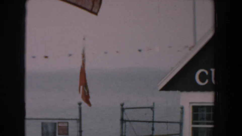 1958 Yorktown, Virginia frame with the building partly out of view, showing a red flag, fence, water and cropped sign lettering.