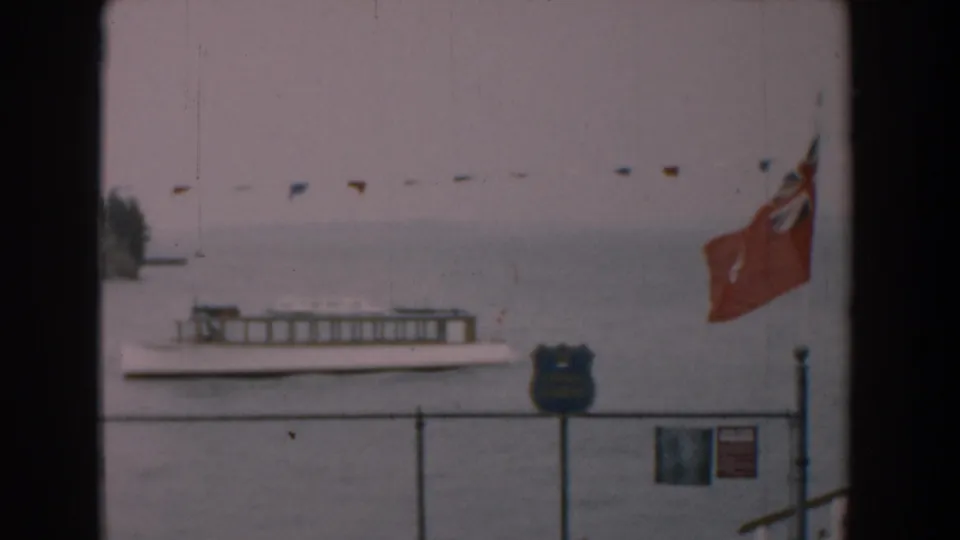 1958 Yorktown waterfront view with the ferry lower in frame, a red Ontario flag, bunting, fence, and public shoreline signs.
