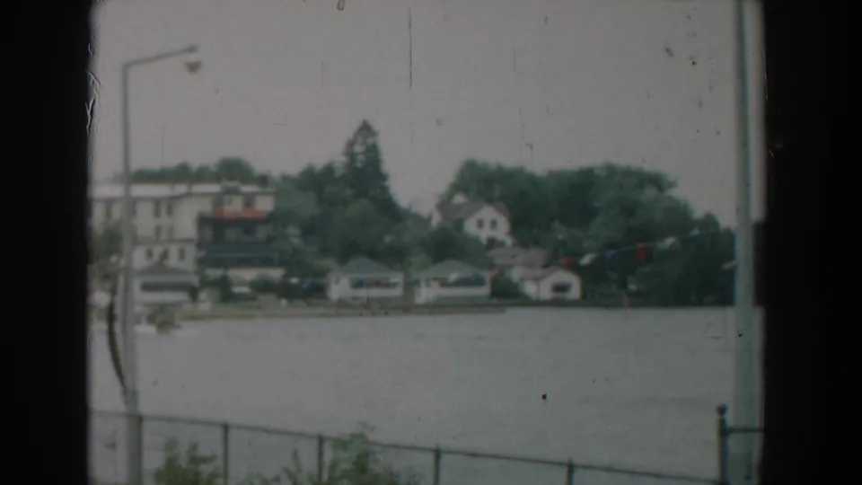 Yorktown, Virginia waterfront scene from 1958 with soft 8mm texture, showing houses, trees, boathouses, water, and a lamp post.