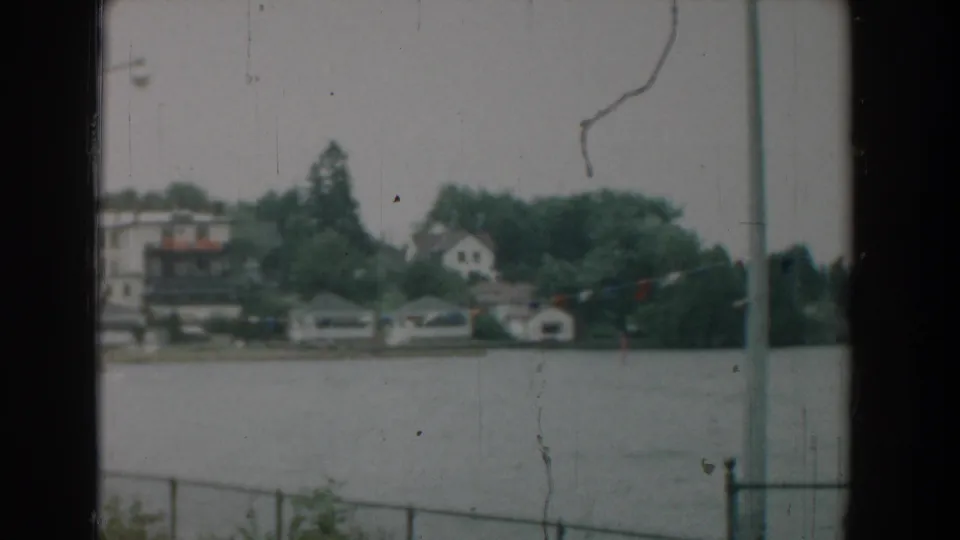 1958 Yorktown waterfront view with houses and boathouses beyond the water, partly framed by a railing and a tall pole.