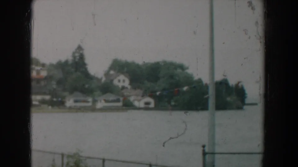 Final 1958 Yorktown frame showing the soft shoreline view across water, with houses, boathouses, trees, railing, and a foreground pole.