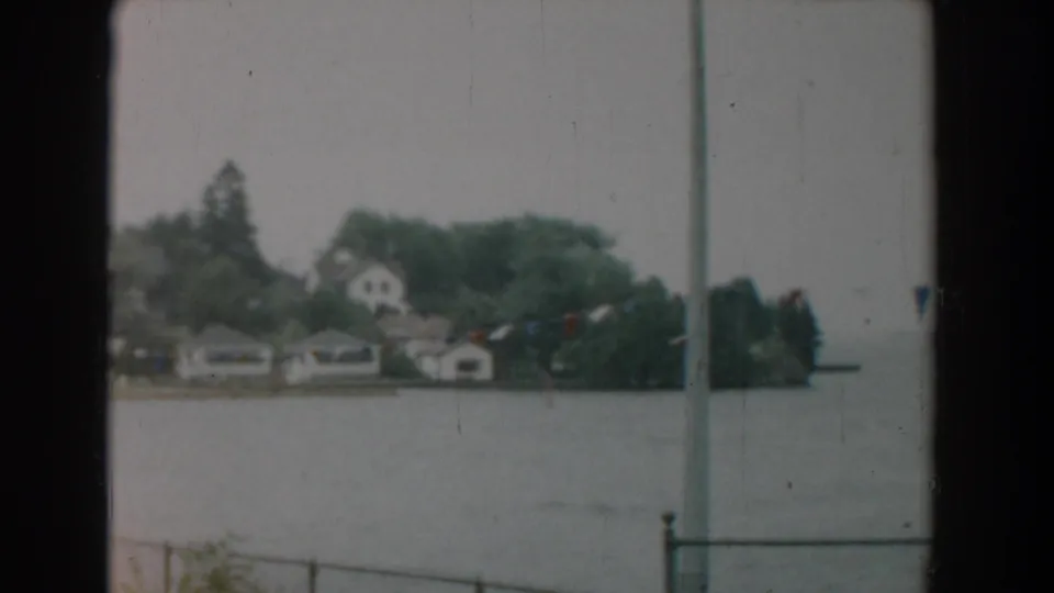 1958 Yorktown, Virginia 8mm frame showing distant waterfront houses, trees, gray water, and a railing or window edge in rainy light.