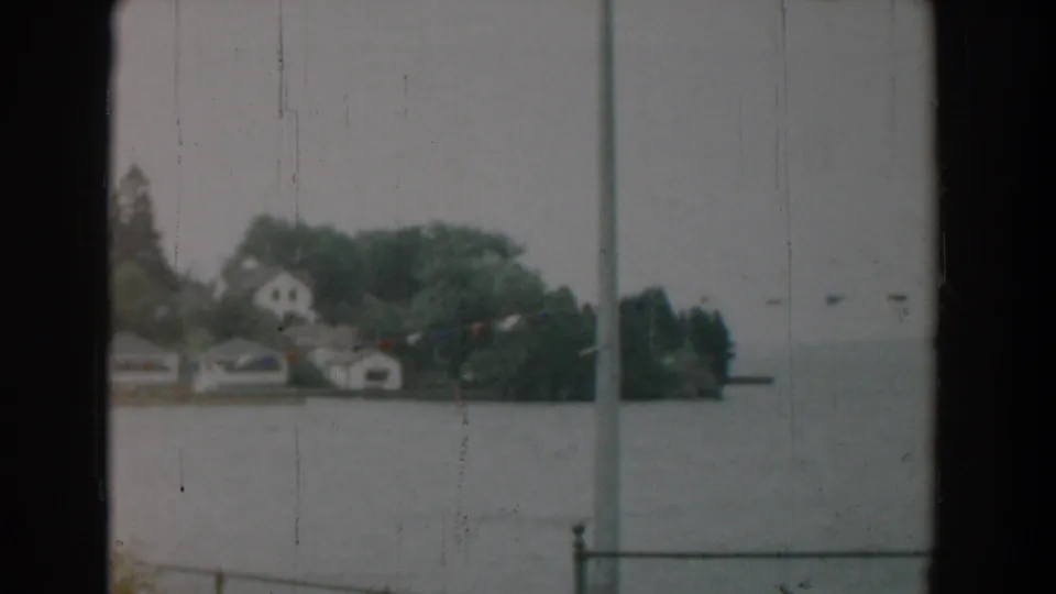 1958 Yorktown waterfront view with houses among trees, muted sky, gray water, and window or railing bars crossing the 8mm frame.