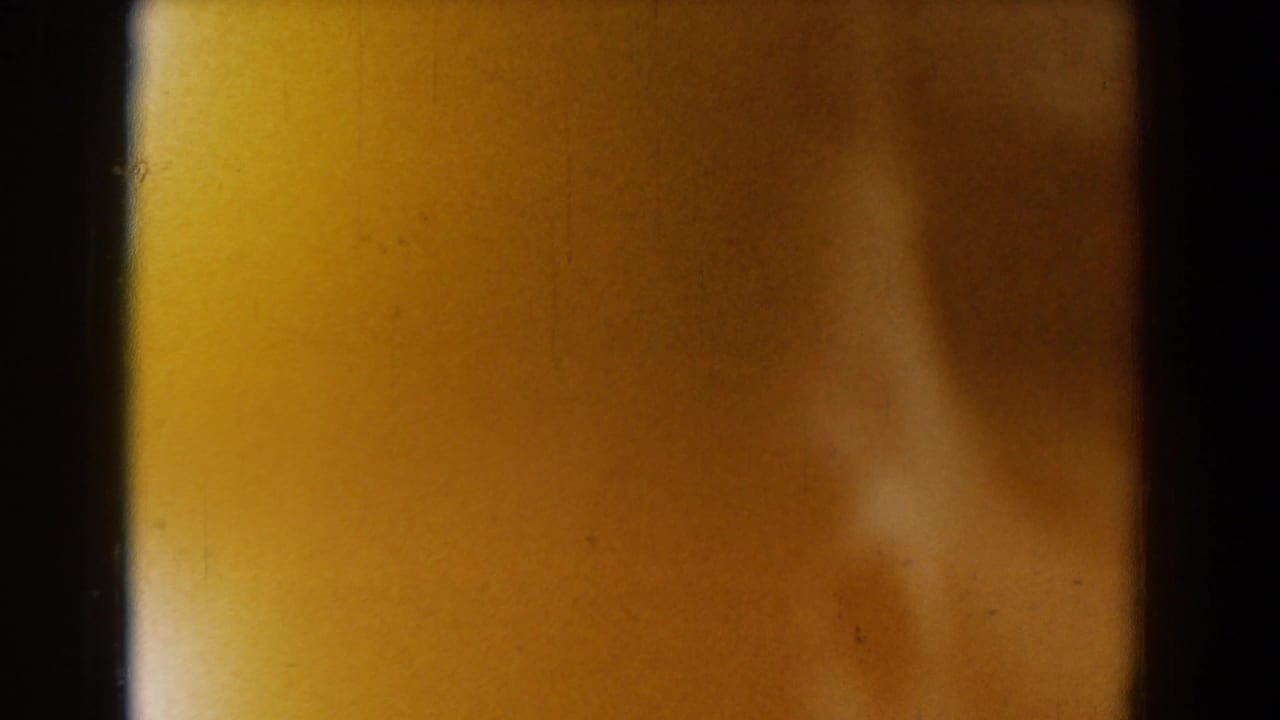 1958 Yorktown 8mm frame with a soft, obscured face-like form behind dark film-strip divisions and warm yellow exposure.
