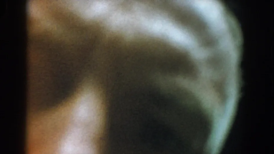 1958 Yorktown 8mm frame showing a dim, green-brown face-like profile obscured by blur, grain, and a dark vertical film edge.
