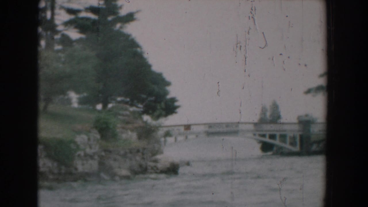 1958 Yorktown, Virginia 8mm view of a low white bridge spanning calm river water beside trees and rocky banks.