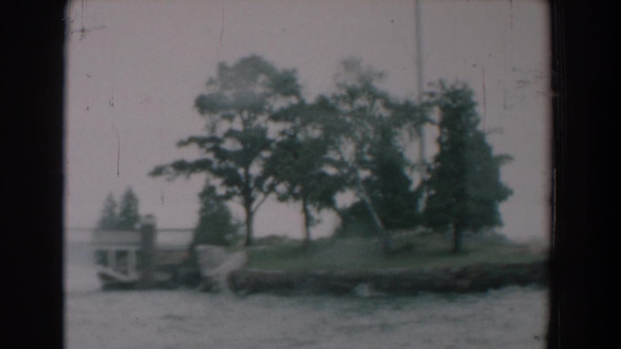 Wooded shoreline point seen across rippling water from a boat.