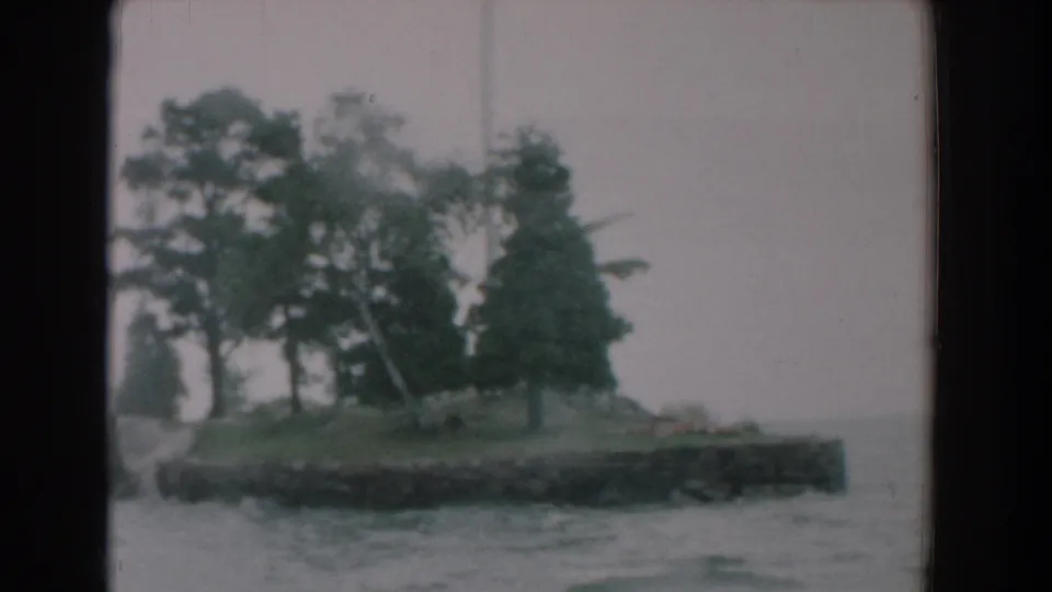 Soft 8mm frame of a tree-covered shoreline or small island seen from a moving boat in Yorktown, Virginia.