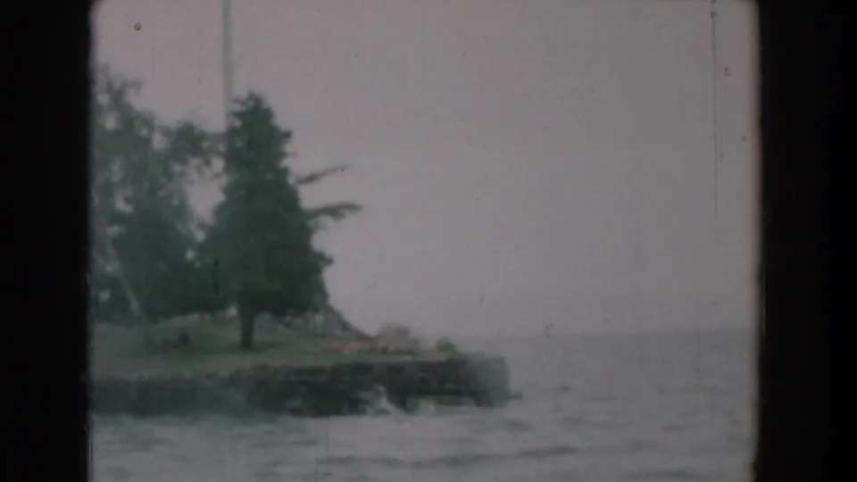 A 1958 boat-view frame shows a tree-lined point and open lake water under a pale sky in Yorktown, Virginia.