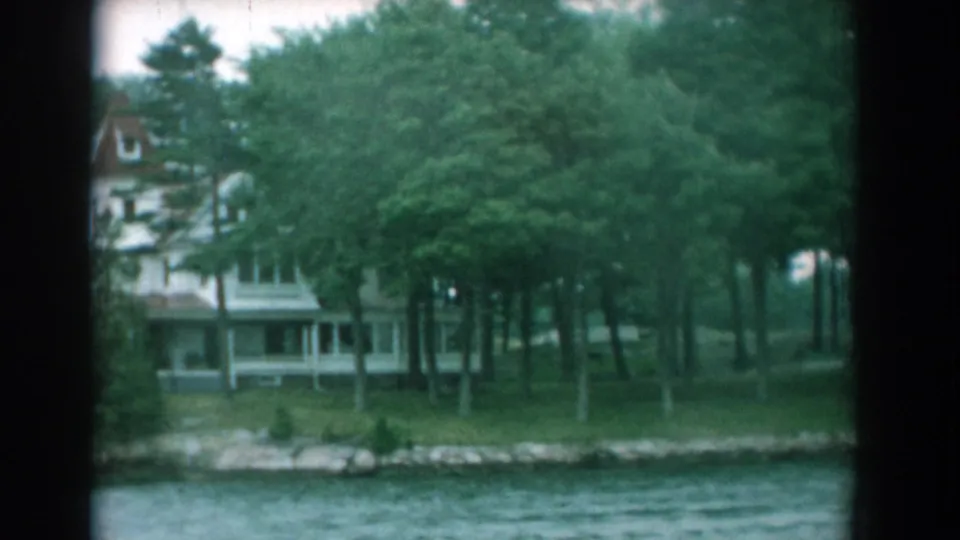 Lakeside house behind tall trees, viewed from the water in 1958 Yorktown, Virginia home-movie footage.