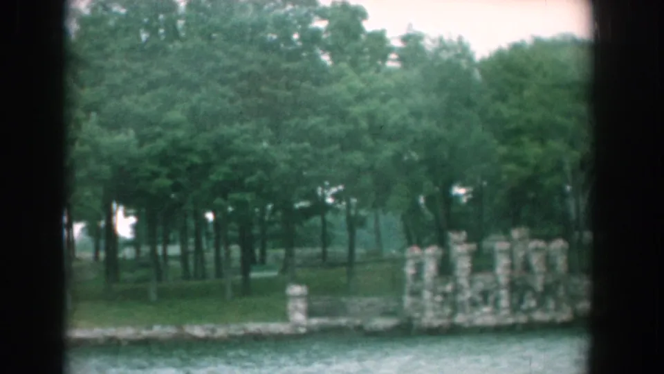 Final 1958 Yorktown boat-view frame with a stone wall, wooded bank, and rippling water in soft 8mm color.