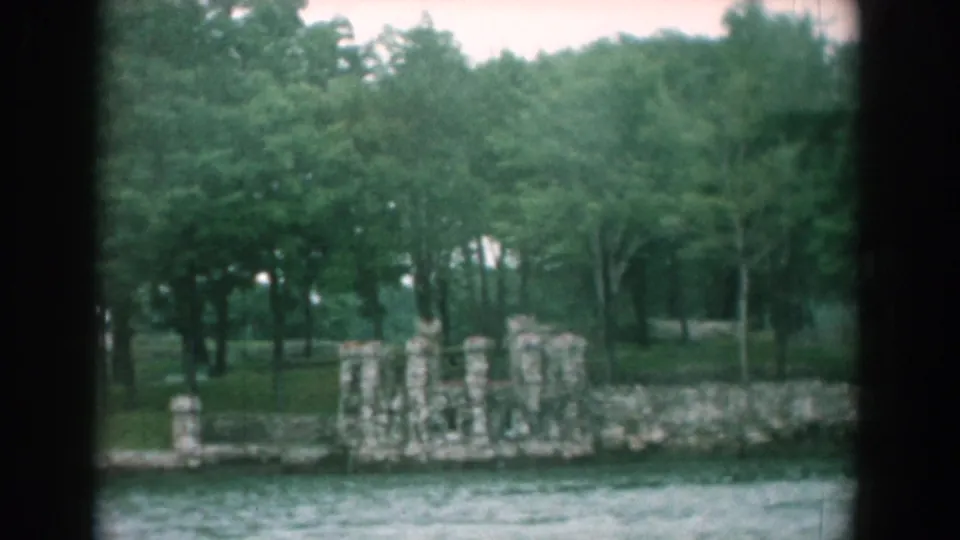 Yorktown, Virginia home-movie frame with stone ruins along the shore and dense green trees behind them.