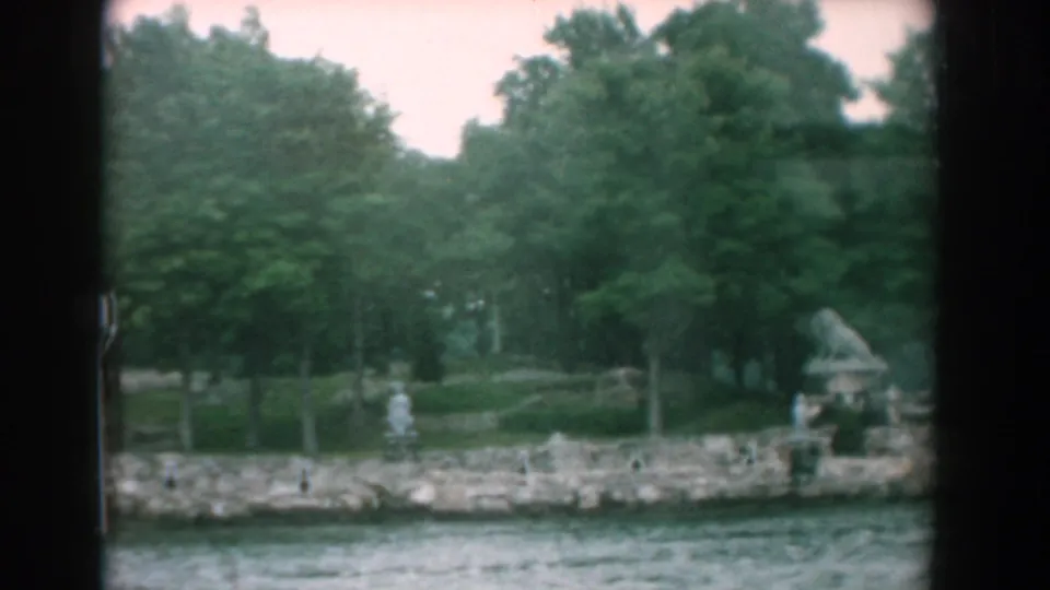 1958 Yorktown, Virginia 8mm frame showing a landscaped riverside garden, stone bank, trees, and small statuary.