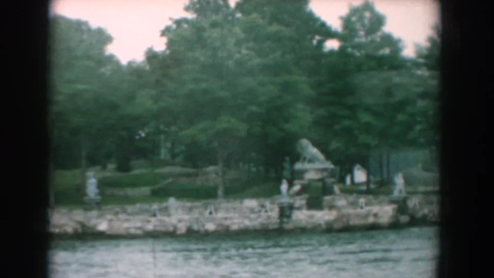 1958 Yorktown, Virginia boat-view frame with rippled water, rocky shoreline, garden statuary, paths, and thick trees.