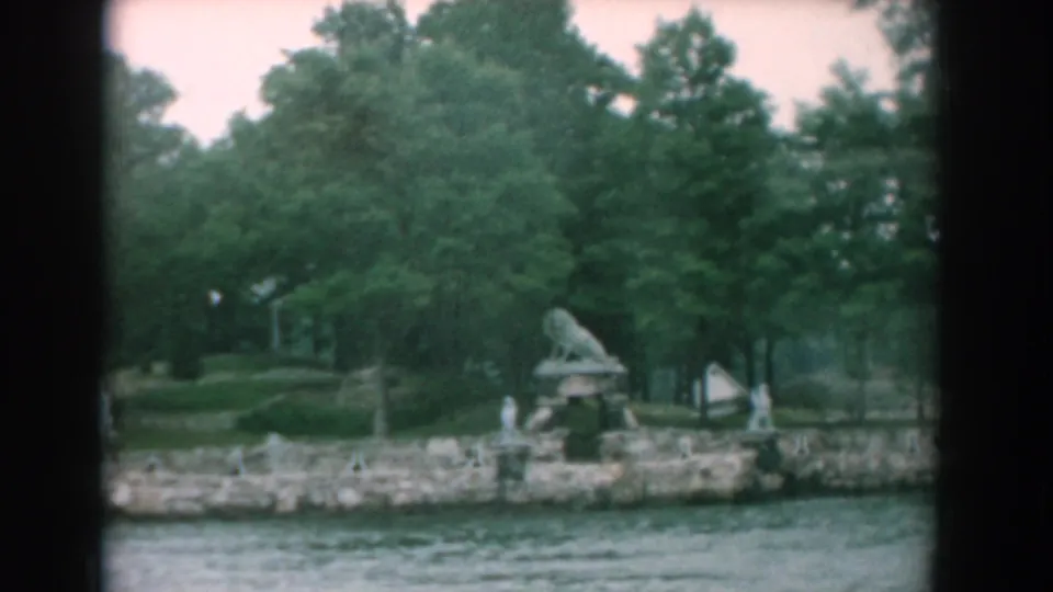 1958 Yorktown waterfront view from a moving boat, showing rippling water, a stone embankment, trees, and a lion sculpture.