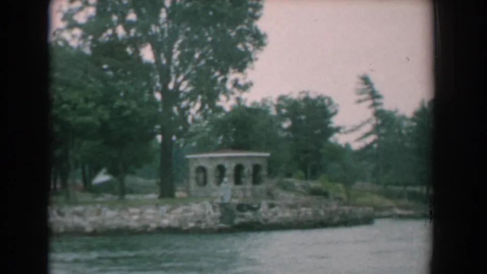 1958 Yorktown riverfront footage showing a gazebo among trees on a rocky shoreline viewed from a boat.