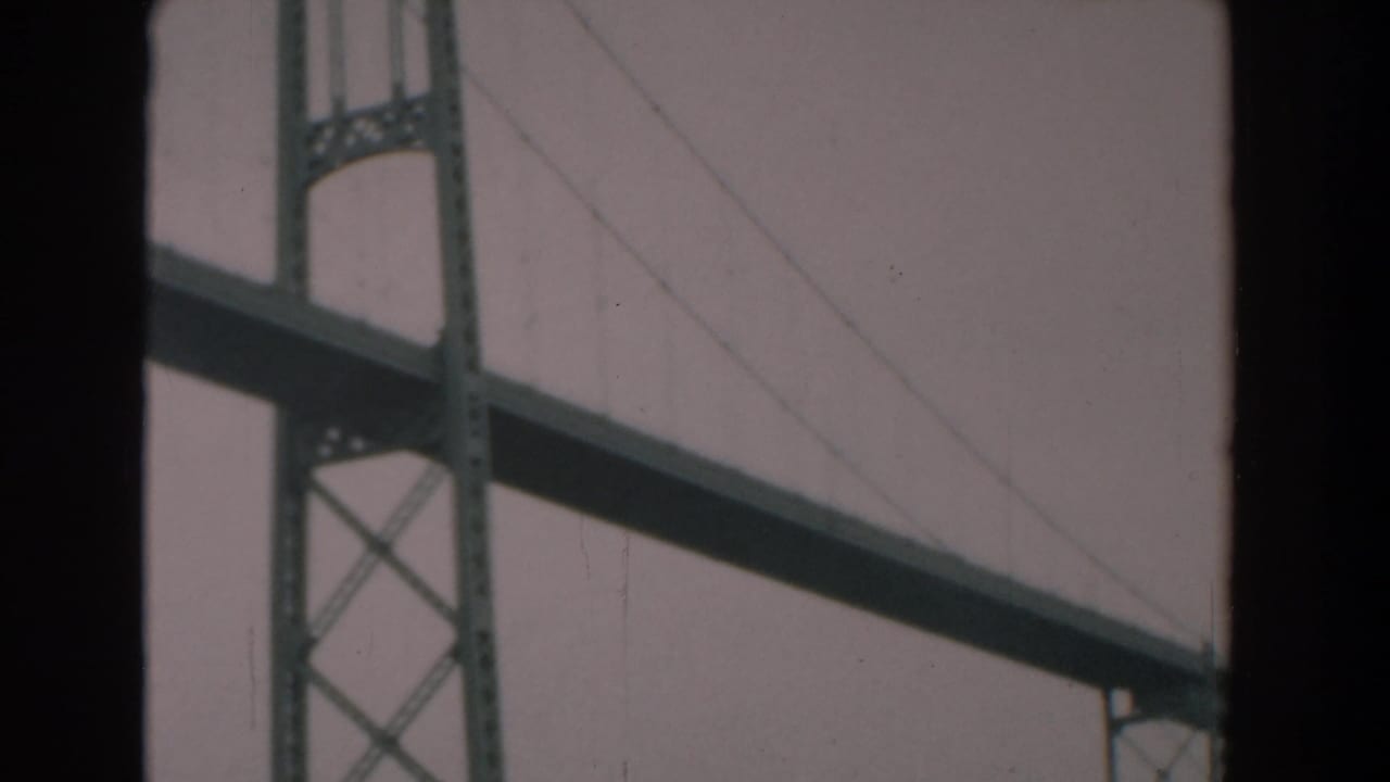 1958 Yorktown, Virginia 8mm frame showing a steel suspension bridge tower, diagonal cables, and overcast sky through dark borders.
