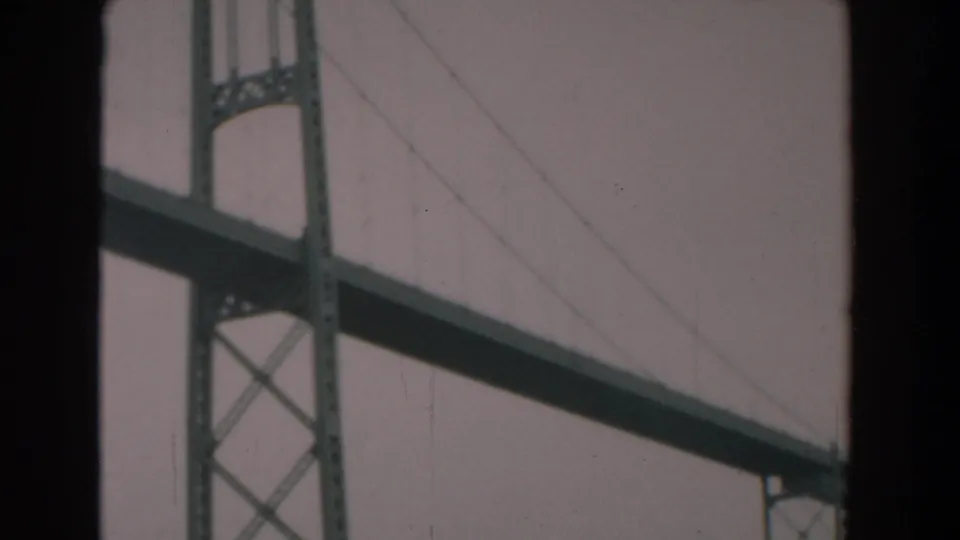 1958 Yorktown, Virginia 8mm frame showing a steel suspension bridge tower, diagonal cables, and overcast sky through dark borders.