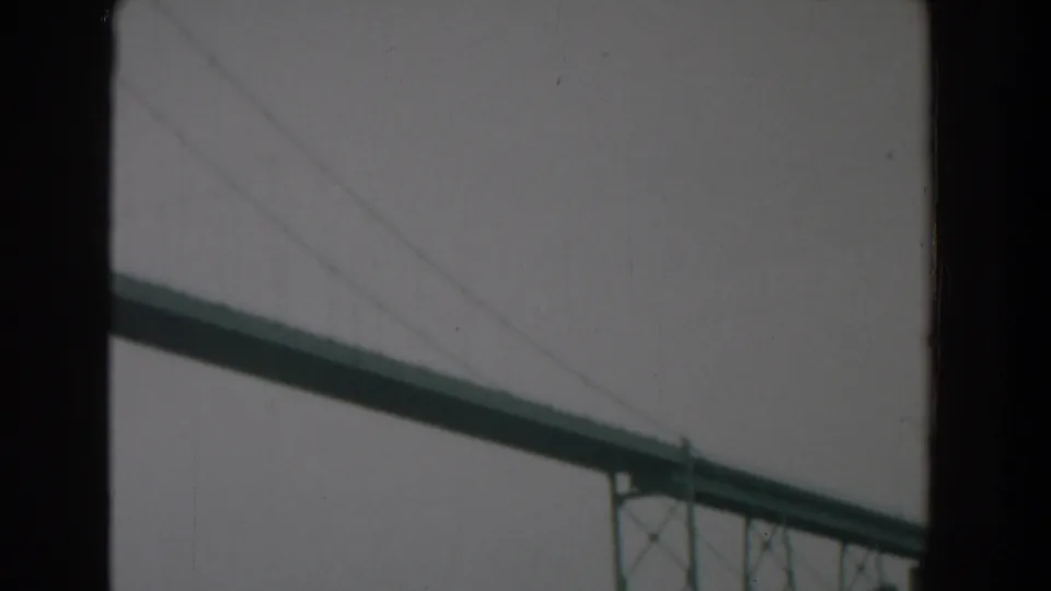 1958 8mm frame from Yorktown showing the long bridge span receding toward a distant tower under a flat gray sky.