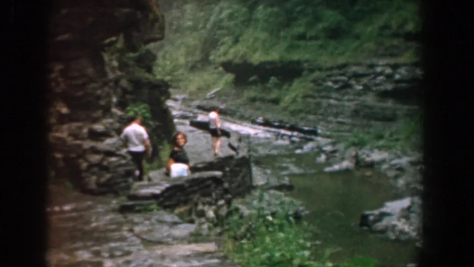 The group continues down the stone path, with one person ahead and two behind near the Yorktown stream.