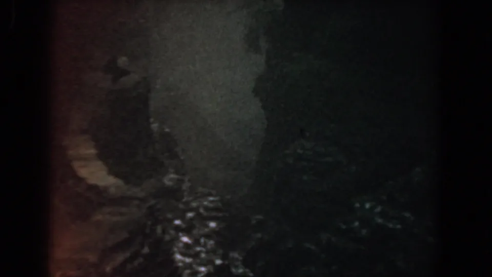 The frame shifts to a darker view of water and rocks, with the walking group no longer clearly visible.