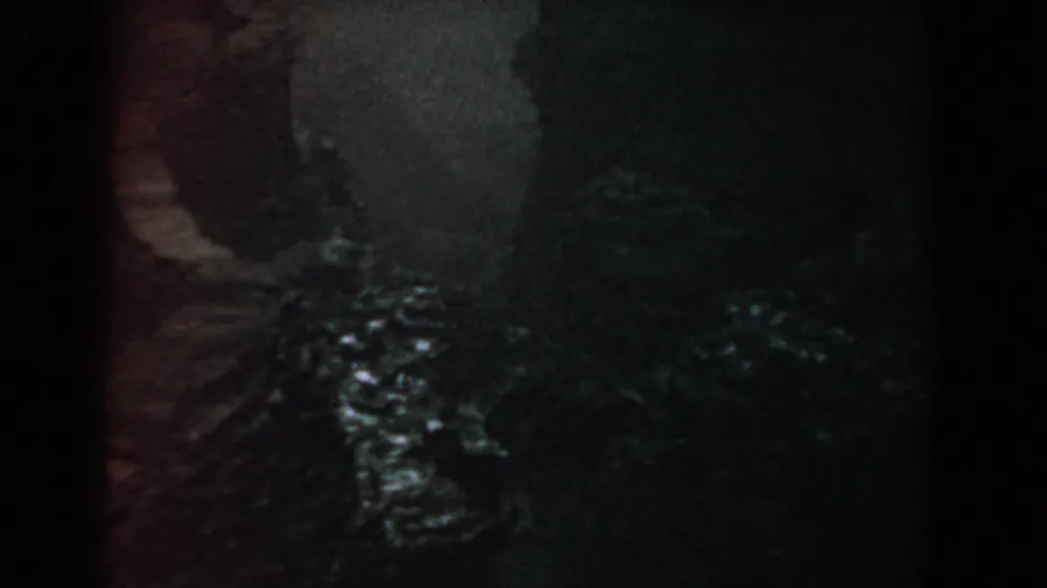 1958 8mm frame from Yorktown, Virginia, appearing to show a dim wooded riverbank or narrow path with glints of water.