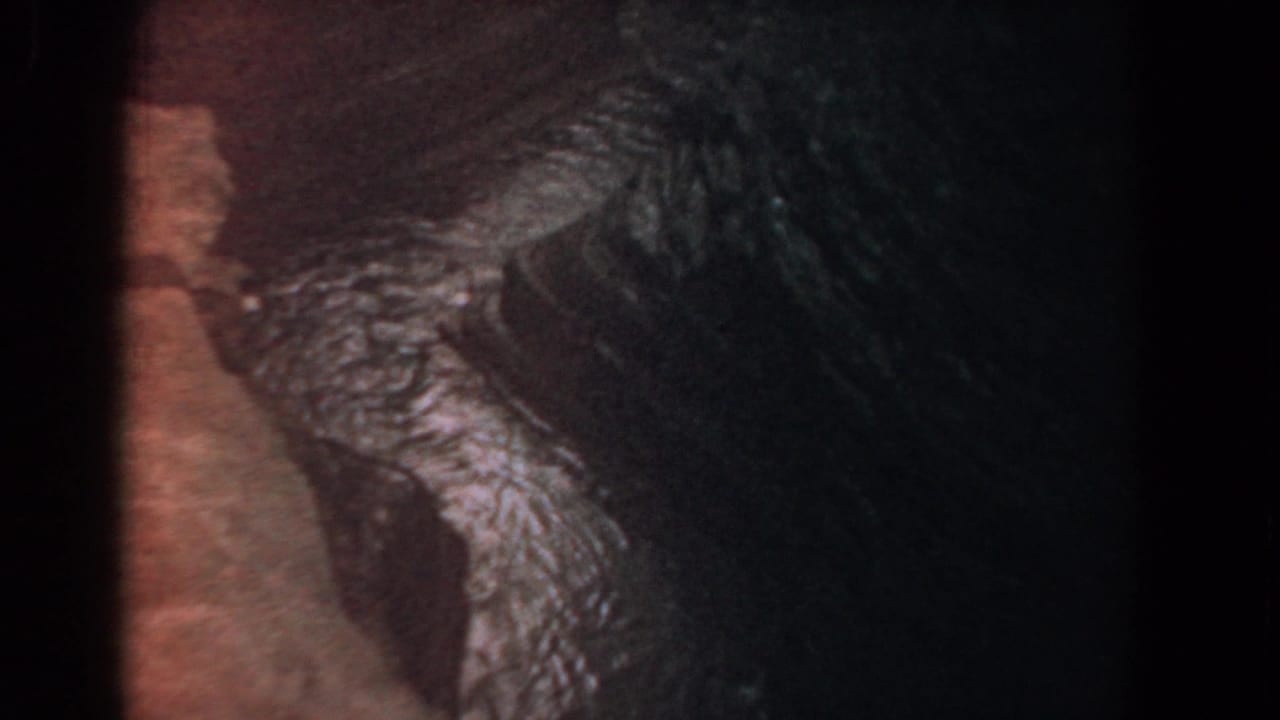 1958 8mm frame attributed to Yorktown showing dark natural texture, reddish-brown edge, and green-blue reflective highlights.