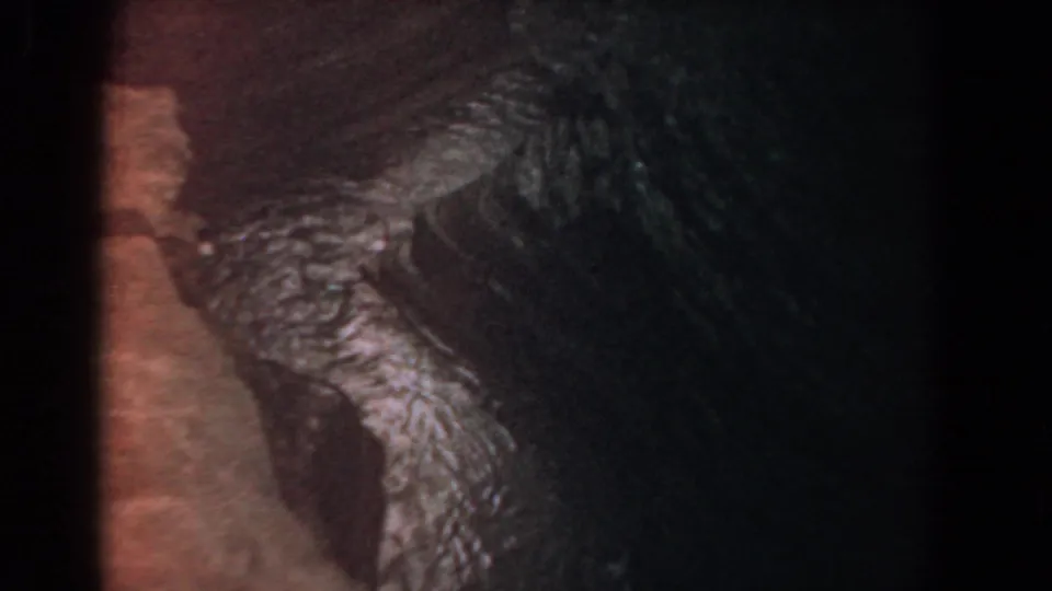 1958 8mm frame attributed to Yorktown showing dark natural texture, reddish-brown edge, and green-blue reflective highlights.