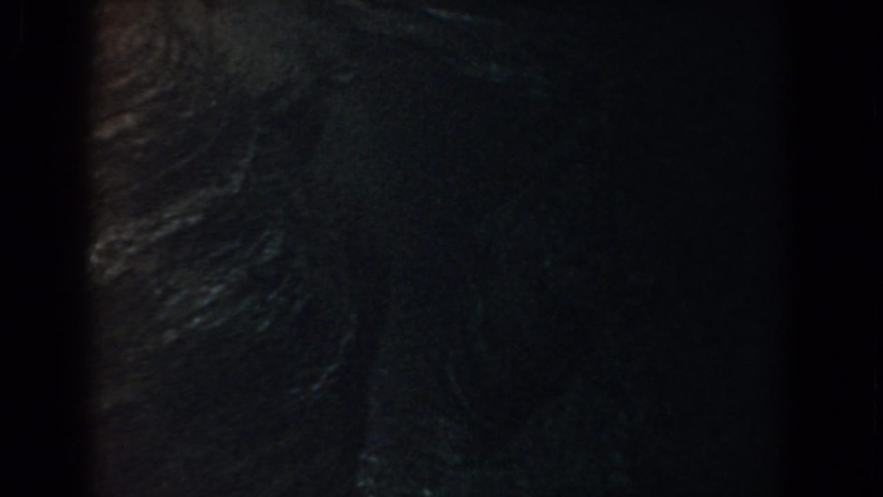 Dark aerial view of ridged terrain with heavy grain and black frame edges.
