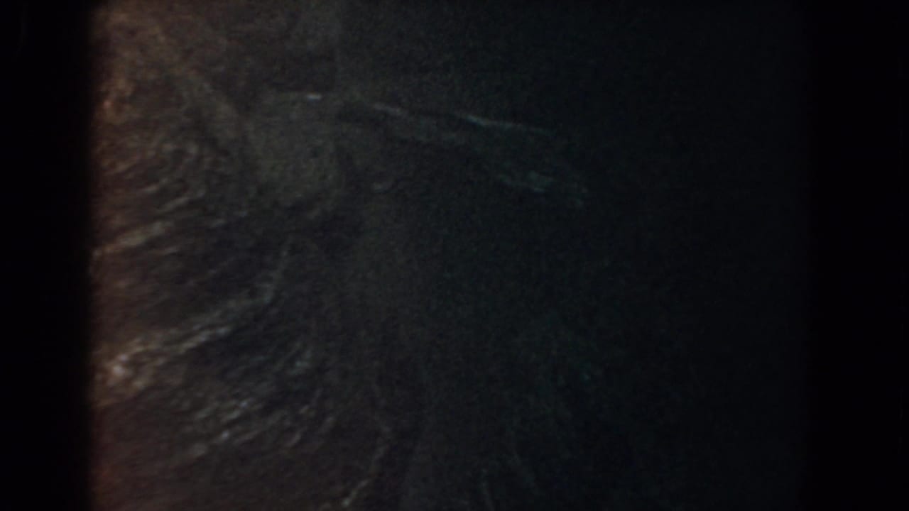Shadowed terrain surface with ridge texture, dim color, and vertical film-edge darkness.