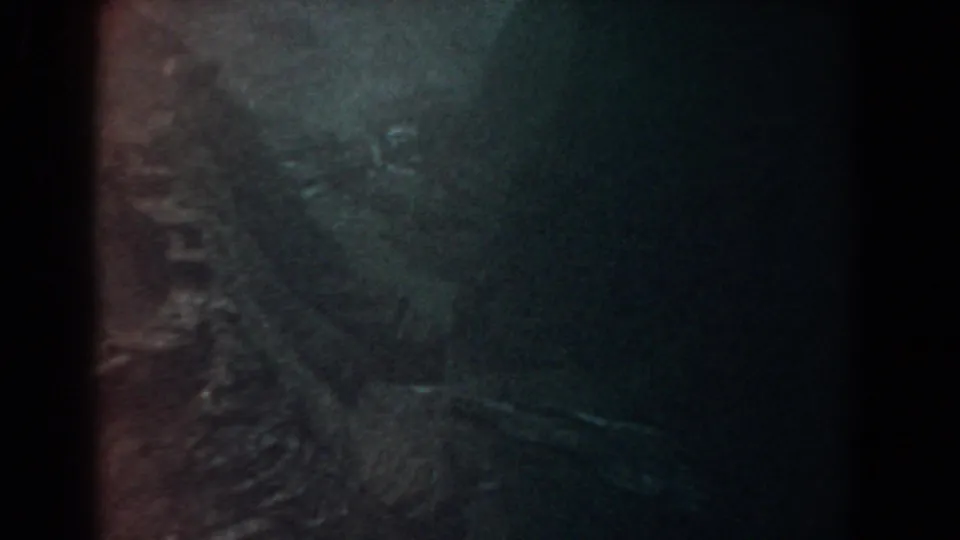 1958 8mm Yorktown footage showing a dim rocky surface with wet texture, deep shadow, and warm edge tinting.